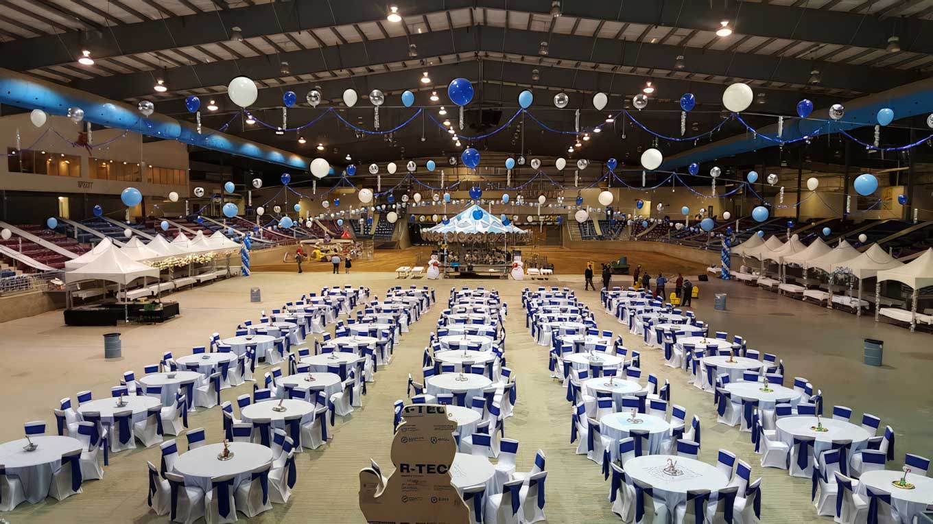 Massive indoor arena transformed with white-and-blue round tables, balloon garlands and canopy tents by Pizazz Rents & Events for a large-scale gala